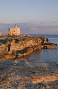 İtalya, Sicilya, Akdeniz, Egadi takımadaları, Favignana Adası (Trapani Eyaleti); gün batımında bir deniz feneri ve adanın kayalık sahili manzarası