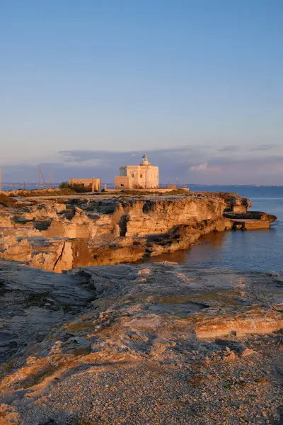 İtalya, Sicilya, Akdeniz, Egadi takımadaları, Favignana Adası (Trapani Eyaleti); gün batımında bir deniz feneri ve adanın kayalık sahili manzarası