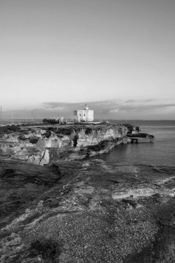 İtalya, Sicilya, Akdeniz, Egadi takımadaları, Favignana Adası (Trapani Eyaleti); gün batımında bir deniz feneri ve adanın kayalık sahili manzarası