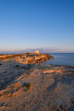 İtalya, Sicilya, Akdeniz, Egadi takımadaları, Favignana Adası (Trapani Eyaleti); gün batımında bir deniz feneri ve adanın kayalık sahili manzarası