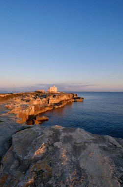 İtalya, Sicilya, Akdeniz, Egadi takımadaları, Favignana Adası (Trapani Eyaleti); gün batımında bir deniz feneri ve adanın kayalık sahili manzarası
