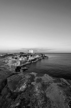 İtalya, Sicilya, Akdeniz, Egadi takımadaları, Favignana Adası (Trapani Eyaleti); gün batımında bir deniz feneri ve adanın kayalık sahili manzarası