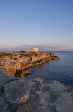 İtalya, Sicilya, Akdeniz, Egadi takımadaları, Favignana Adası (Trapani Eyaleti); gün batımında bir deniz feneri ve adanın kayalık sahili manzarası