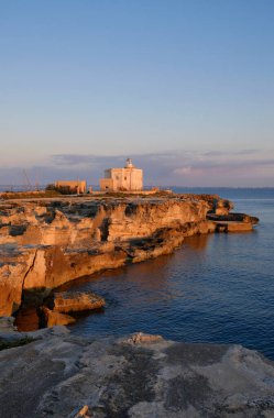 İtalya, Sicilya, Akdeniz, Egadi takımadaları, Favignana Adası (Trapani Eyaleti); gün batımında bir deniz feneri ve adanın kayalık sahili manzarası