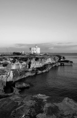 İtalya, Sicilya, Akdeniz, Egadi takımadaları, Favignana Adası (Trapani Eyaleti); gün batımında bir deniz feneri ve adanın kayalık sahili manzarası