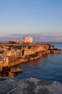 İtalya, Sicilya, Akdeniz, Egadi takımadaları, Favignana Adası (Trapani Eyaleti); gün batımında bir deniz feneri ve adanın kayalık sahili manzarası