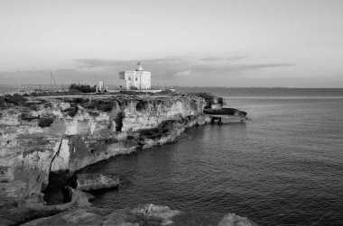 İtalya, Sicilya, Akdeniz, Egadi takımadaları, Favignana Adası (Trapani Eyaleti); gün batımında bir deniz feneri ve adanın kayalık sahili manzarası