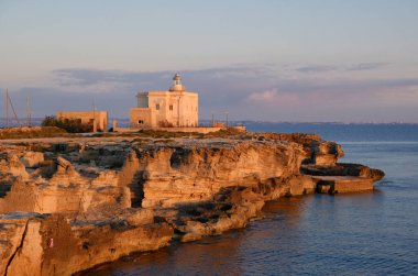 İtalya, Sicilya, Akdeniz, Egadi takımadaları, Favignana Adası (Trapani Eyaleti); gün batımında bir deniz feneri ve adanın kayalık sahili manzarası