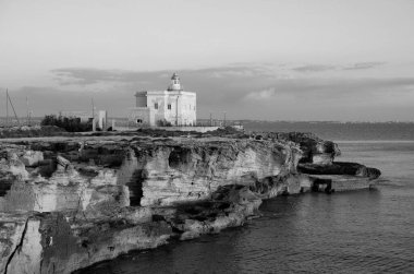 İtalya, Sicilya, Akdeniz, Egadi takımadaları, Favignana Adası (Trapani Eyaleti); gün batımında bir deniz feneri ve adanın kayalık sahili manzarası