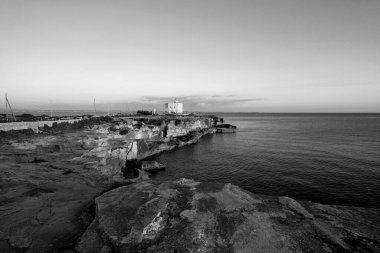 İtalya, Sicilya, Akdeniz, Egadi takımadaları, Favignana Adası (Trapani Eyaleti); gün batımında bir deniz feneri ve adanın kayalık sahili manzarası