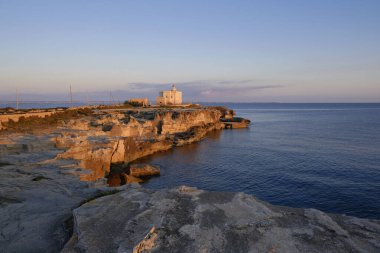 İtalya, Sicilya, Akdeniz, Egadi takımadaları, Favignana Adası (Trapani Eyaleti); gün batımında bir deniz feneri ve adanın kayalık sahili manzarası