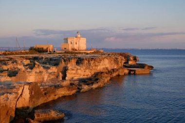 İtalya, Sicilya, Akdeniz, Egadi takımadaları, Favignana Adası (Trapani Eyaleti); gün batımında bir deniz feneri ve adanın kayalık sahili manzarası