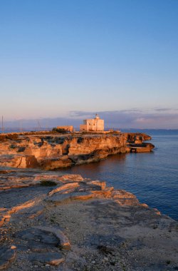 İtalya, Sicilya, Akdeniz, Egadi takımadaları, Favignana Adası (Trapani Eyaleti); gün batımında bir deniz feneri ve adanın kayalık sahili manzarası