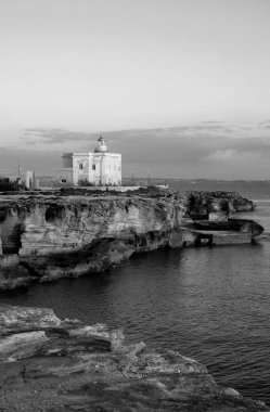 İtalya, Sicilya, Akdeniz, Egadi takımadaları, Favignana Adası (Trapani Eyaleti); gün batımında bir deniz feneri ve adanın kayalık sahili manzarası