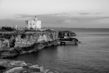 İtalya, Sicilya, Akdeniz, Egadi takımadaları, Favignana Adası (Trapani Eyaleti); gün batımında bir deniz feneri ve adanın kayalık sahili manzarası