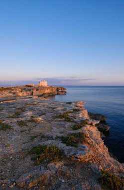 İtalya, Sicilya, Akdeniz, Egadi takımadaları, Favignana Adası (Trapani Eyaleti); gün batımında bir deniz feneri ve adanın kayalık sahili manzarası
