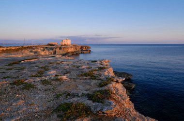 İtalya, Sicilya, Akdeniz, Egadi takımadaları, Favignana Adası (Trapani Eyaleti); gün batımında bir deniz feneri ve adanın kayalık sahili manzarası