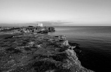 İtalya, Sicilya, Akdeniz, Egadi takımadaları, Favignana Adası (Trapani Eyaleti); gün batımında bir deniz feneri ve adanın kayalık sahili manzarası