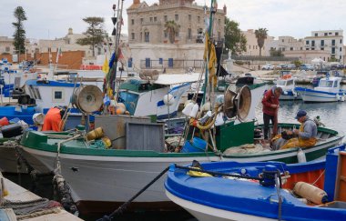 İtalya, Sicilya, Akdeniz, Egadi takımadaları, Favignana Adası (Trapani Eyaleti); 22 Mart 2024, balıkçılar, balıkçılar, balıkçı tekneleri ve ağlar limanda (arkada Florio Sarayı) - EDITORIAL