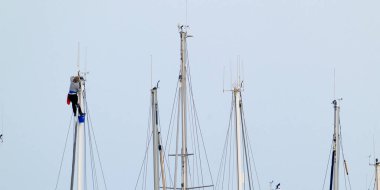 İtalya, Sicilya, Akdeniz, Marina di Ragusa (Ragusa Eyaleti), limanda bir katamaran yelkenli direğine tırmanan kadın.