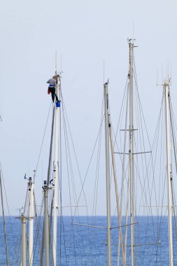 İtalya, Sicilya, Akdeniz, Marina di Ragusa (Ragusa Eyaleti), limanda bir katamaran yelkenli direğine tırmanan kadın.