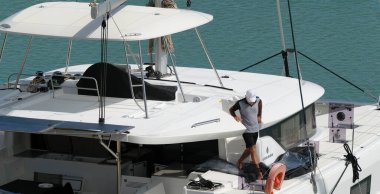 İtalya, Sicilya, Akdeniz, Marina di Ragusa (Ragusa Eyaleti); 21 Nisan 2024, limandaki bir katamaran yelkenli teknesinde adam - EDITORIAL