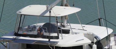 İtalya, Sicilya, Akdeniz, Marina di Ragusa (Ragusa Eyaleti), limandaki katamaran yelkenli teknesinde bir adam. 