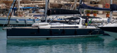 İtalya, Sicilya, Akdeniz, Marina di Ragusa (Ragusa ili); 7 Temmuz 2024, limanda bir yelkenli ve lüks yatlarda erkekler - EDITORIAL