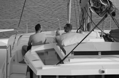 İtalya, Sicilya, Akdeniz, Marina di Ragusa (Ragusa Eyaleti); limandaki katamaran yelkenli teknesinde erkekler 