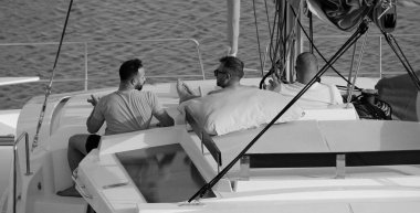 İtalya, Sicilya, Akdeniz, Marina di Ragusa (Ragusa Eyaleti); limandaki katamaran yelkenli teknesinde erkekler 