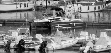 İtalya, Sicilya, Akdeniz, Marina di Ragusa (Ragusa ili); 11 Temmuz 2024, limandaki bir trimaran yelkenli teknesi ve lüks yatlarda yaşayan insanlar - EDITORIAL