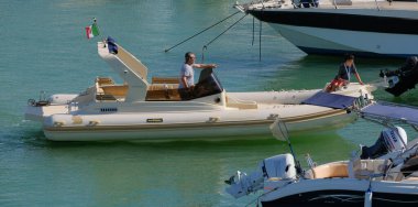 İtalya, Sicilya, Akdeniz, Marina di Ragusa (Ragusa Eyaleti); 12 Temmuz 2024, büyük bir kauçuk bot ve limandaki lüks yatlarda yaşayan insanlar - EDITORIAL