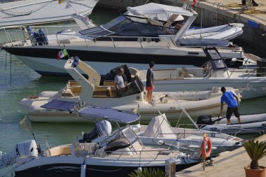 İtalya, Sicilya, Akdeniz, Marina di Ragusa (Ragusa Eyaleti); 12 Temmuz 2024, büyük bir kauçuk bot ve limandaki lüks yatlarda yaşayan insanlar - EDITORIAL