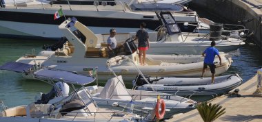 İtalya, Sicilya, Akdeniz, Marina di Ragusa (Ragusa Eyaleti); 12 Temmuz 2024, büyük bir kauçuk bot ve limandaki lüks yatlarda yaşayan insanlar - EDITORIAL