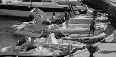 İtalya, Sicilya, Akdeniz, Marina di Ragusa (Ragusa Eyaleti); 12 Temmuz 2024, büyük bir kauçuk bot ve limandaki lüks yatlarda yaşayan insanlar - EDITORIAL