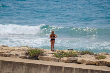 İtalya, Sicilya, Akdeniz, Marina di Ragusa (Ragusa Eyaleti), deniz kenarındaki kayalıklarda duran kadın