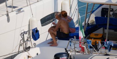 İtalya, Sicilya, Akdeniz, Marina di Ragusa (Ragusa Eyaleti); 5 Ağustos 2024, limanda bir katamaran yelkenli teknesinde çift