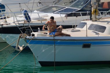 İtalya, Sicilya, Akdeniz, Marina di Ragusa (Ragusa Eyaleti); 6 Ağustos 2024, limandaki bir yelkenli teknesinde adam - EDITORIAL