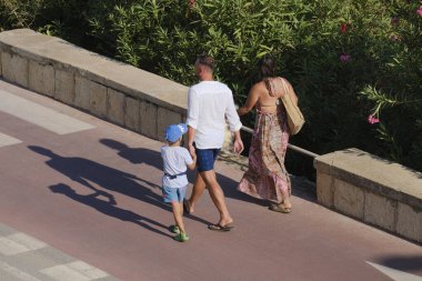 İtalya, Sicilya, Akdeniz, Marina di Ragusa (Ragusa Eyaleti), deniz kenarında bisiklet yolunda yürüyen aile.