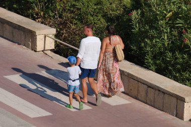 İtalya, Sicilya, Akdeniz, Marina di Ragusa (Ragusa Eyaleti), deniz kenarında bisiklet yolunda yürüyen aile.
