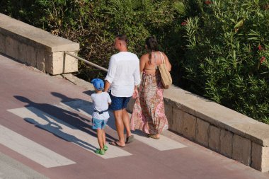 İtalya, Sicilya, Akdeniz, Marina di Ragusa (Ragusa Eyaleti), deniz kenarında bisiklet yolunda yürüyen aile.