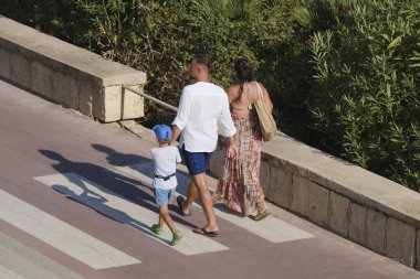 İtalya, Sicilya, Akdeniz, Marina di Ragusa (Ragusa Eyaleti), deniz kenarında bisiklet yolunda yürüyen aile.