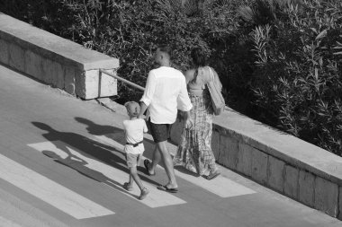İtalya, Sicilya, Akdeniz, Marina di Ragusa (Ragusa Eyaleti), deniz kenarında bisiklet yolunda yürüyen aile.