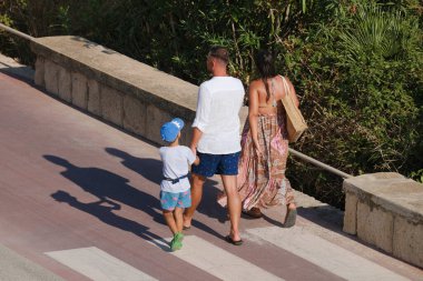 İtalya, Sicilya, Akdeniz, Marina di Ragusa (Ragusa Eyaleti), deniz kenarında bisiklet yolunda yürüyen aile.