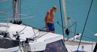 İtalya, Sicilya, Akdeniz, Marina di Ragusa (Ragusa Eyaleti); 16 Eylül 2024, limanda katamaran yelkenli teknesini temizleyen adam - EDITORIAL