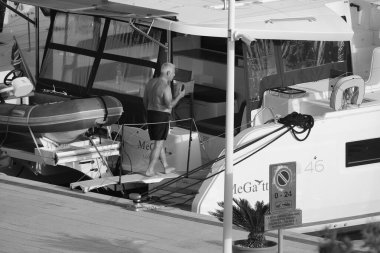 İtalya, Sicilya, Akdeniz, Marina di Ragusa (Ragusa Eyaleti); 3 Ekim 2024, limandaki bir katamaran yelkenli teknesinde adam - EDITORIAL