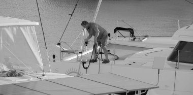 İtalya, Sicilya, Akdeniz, Marina di Ragusa (Ragusa Eyaleti); 4 Ekim 2024, limandaki bir katamaran yelkenli teknesinde adam - EDITORIAL