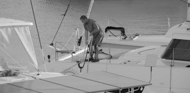 İtalya, Sicilya, Akdeniz, Marina di Ragusa (Ragusa Eyaleti); 4 Ekim 2024, limandaki bir katamaran yelkenli teknesinde adam - EDITORIAL