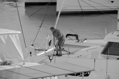 İtalya, Sicilya, Akdeniz, Marina di Ragusa (Ragusa Eyaleti); 4 Ekim 2024, limandaki bir katamaran yelkenli teknesinde adam - EDITORIAL