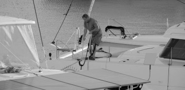 İtalya, Sicilya, Akdeniz, Marina di Ragusa (Ragusa Eyaleti); 4 Ekim 2024, limandaki bir katamaran yelkenli teknesinde adam - EDITORIAL